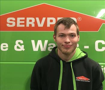 Male employee with blonde hair standing in front of a green Servpro vehicle