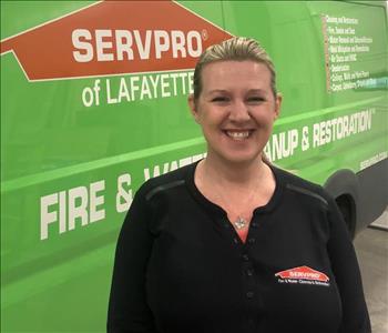 Female employee with blonde hair standing in front of a green Servpro vehicle