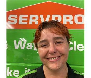 Female employee with strawberry blonde hair standing in front of a green Servpro vehicle
