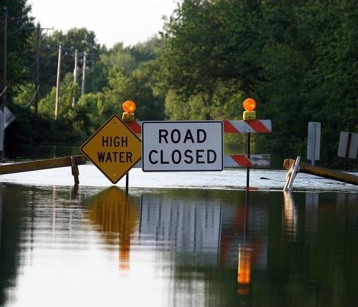 Water covering road; ‘Road Closed’ and ‘High Water’ sign in middle of street