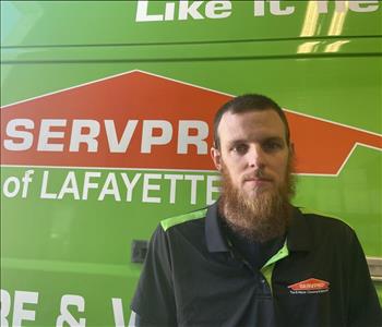 Young man with abeard, standing in front of a green Servpro work vehicle