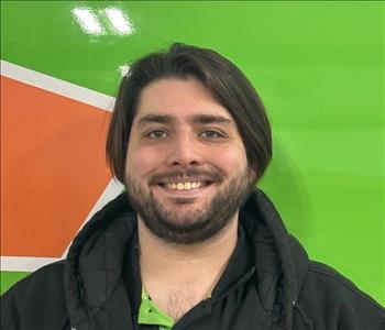 Young man with straight brown hair smiling in front of a green work van