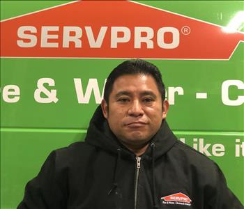 Male employee wearing a baseball cap standing in front of a green Servpro vehicle